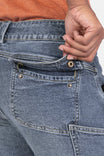 Detail view of the back pocket and waistband of Dovetail Workwear's Day Construct Work Pant in Vintage Blue Stretch Denim, shown on a woman wearing an orange top