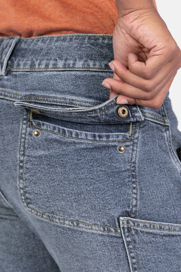 Detail view of the back pocket and waistband of Dovetail Workwear's Day Construct Work Pant in Vintage Blue Stretch Denim, shown on a woman wearing an orange top