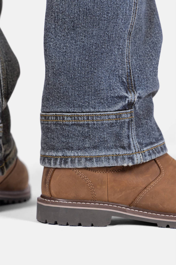 Detail shot of the Day Construct Work Pant in Vintage Blue Stretch Denim by Dovetail Workwear, showing the relaxed leg hem and reinforced knee pad slot on a woman wearing tan work boots