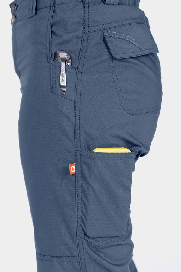 Side view of a woman wearing the Dovetail Workwear Day X COOLSWAP™ Pant in Dovetail Blue, showing multiple pockets and the phone pocket detail