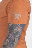Side view of a woman wearing the Dovetail Workwear GO TO™ "Get Dirty" Graphic Work Tee in rust orange with graphic logo, paired with dark patterned sleeve tattoo