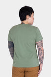 Back view of a woman wearing the Dovetail Workwear GO TO™ "Work Like a Mother" Graphic Work Tee in sage green with brown pants, showcasing the relaxed fit and cotton jersey blend fabric