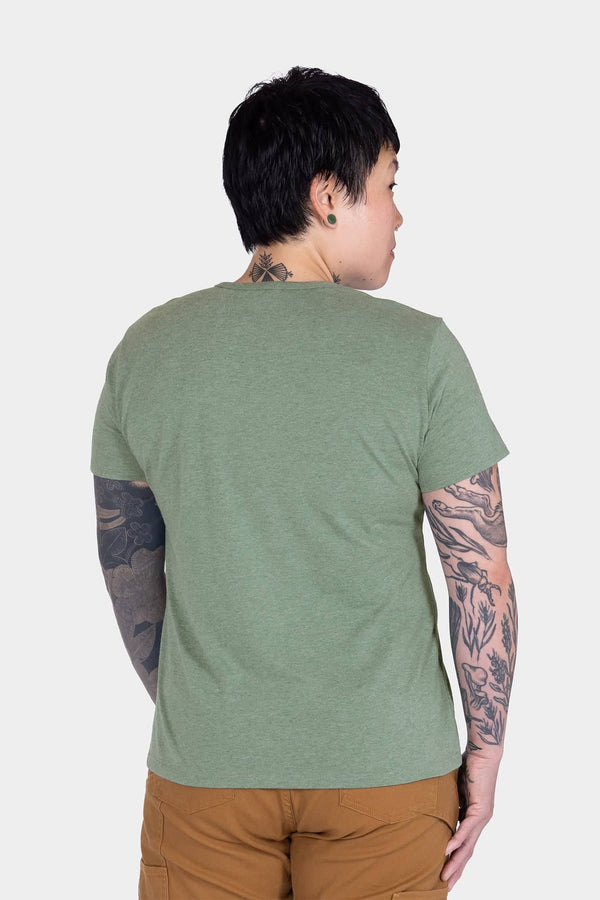 Back view of a woman wearing the Dovetail Workwear GO TO™ "Work Like a Mother" Graphic Work Tee in sage green with brown pants, showcasing the relaxed fit and cotton jersey blend fabric