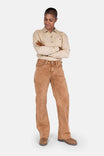 Woman wearing Dovetail Workwear's Old School Wide Leg Mineral Wash Jeans in Sunbaked Copper with a beige button-up shirt, arms crossed, looking down
