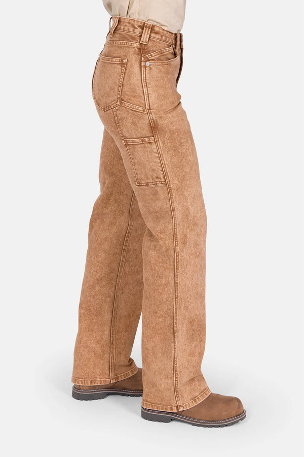 Side view of a woman wearing Dovetail Workwear's Old School Wide Leg Mineral Wash Jeans in Sunbaked Copper, featuring nested side pockets and a high-rise fit with wide leg silhouette