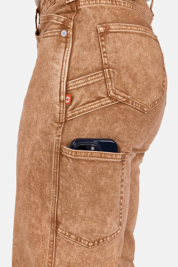 Side view of a woman wearing Dovetail Workwear's Old School Wide Leg Mineral Wash Jeans in Sunbaked Copper, highlighting the nested side pockets and phone pocket with a smartphone visible