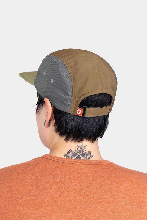 Back view of a woman wearing the Dovetail Workwear Pack Cap in Desert Tan, showcasing the adjustable back closure and side ventilation ports