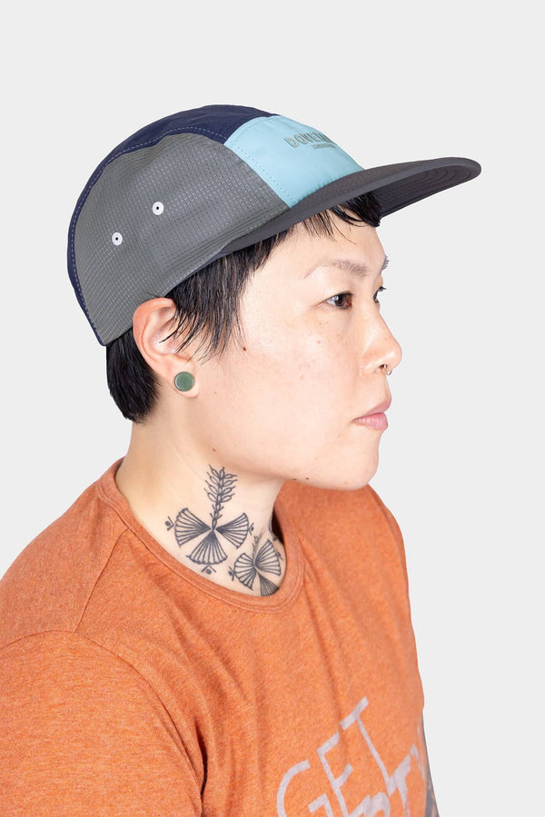 Side profile of a woman wearing the Dovetail Workwear Pack Cap in Ocean Blue, showcasing the 5-panel construction and adjustable back closure