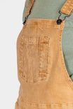 Detail view of the Tan Sandstone Utility Short Overalls by Dovetail Workwear, showing the bib pocket with snap closure and Hip Clip on a woman wearing a sage green shirt