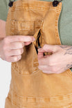 Detail view of the hidden zip pocket on Dovetail Workwear's Utility Short Overalls in Tan Sandstone, shown being opened by a woman's hands