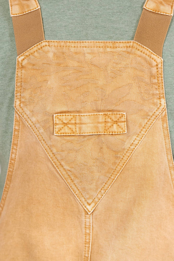 Detail shot of the Utility Short Overalls in Tan Sandstone by Dovetail Workwear, showing the bib pocket with snap closure and jacquard botanical texture print