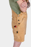 Side view of a woman wearing Dovetail Workwear Utility Short Overalls in Tan Sandstone, displaying multiple pockets, snap closures, and tool loops