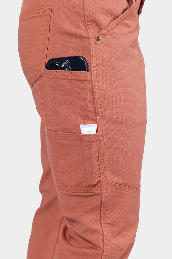 Side view of a woman wearing Dovetail Workwear GO TO™ Pants in Terracotta, displaying nested pockets and tool loop with phone in pocket