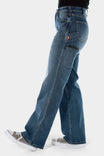 Side view of a woman wearing Dovetail Workwear's Old School Wide Leg Jeans in Classic Indigo Blue, featuring visible thigh pocket and wide leg silhouette
