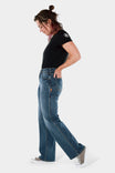 Side view of a woman wearing Dovetail Workwear's Old School Wide Leg Jeans in Classic Indigo Blue denim, showcasing the high-rise fit and wide leg silhouette with visible thigh pocket detail