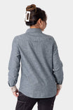 Back view of a woman wearing the Dovetail Workwear Givens Long Sleeve Summer Work Shirt in Indigo Blue, showing the shaped fit and contrast cuff tabs.