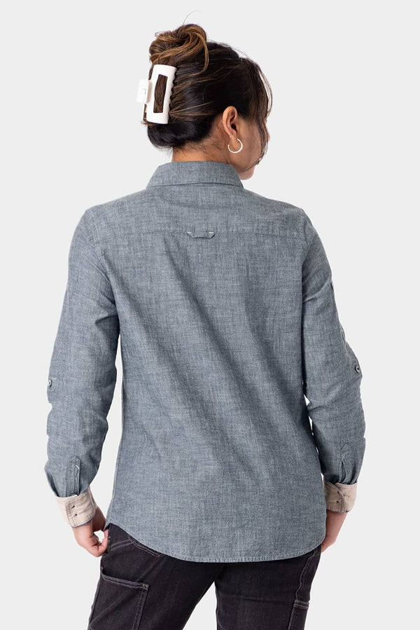 Back view of a woman wearing the Dovetail Workwear Givens Long Sleeve Summer Work Shirt in Indigo Blue, showing the shaped fit and contrast cuff tabs.