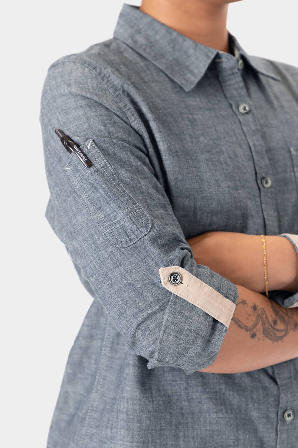 Woman wearing Dovetail Workwear's Givens Long Sleeve Summer Work Shirt in Indigo Blue, highlighting the button chest pocket, sleeve pencil pocket, and contrast cuff details.