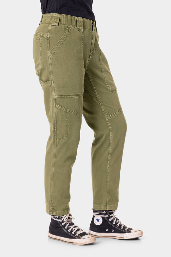Side view of a woman wearing Dovetail Workwear's Range Crop Pant in Kelp Green, featuring bellowed front pockets and a cropped inseam, paired with black canvas sneakers