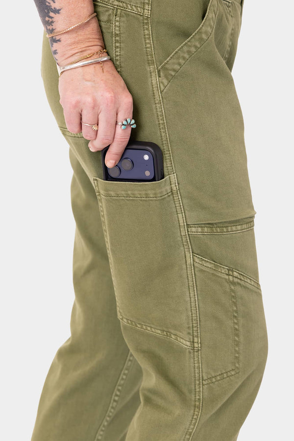 Woman wearing Dovetail Workwear Range Crop Pant in Kelp Green, demonstrating the bellowed front pocket while holding a phone