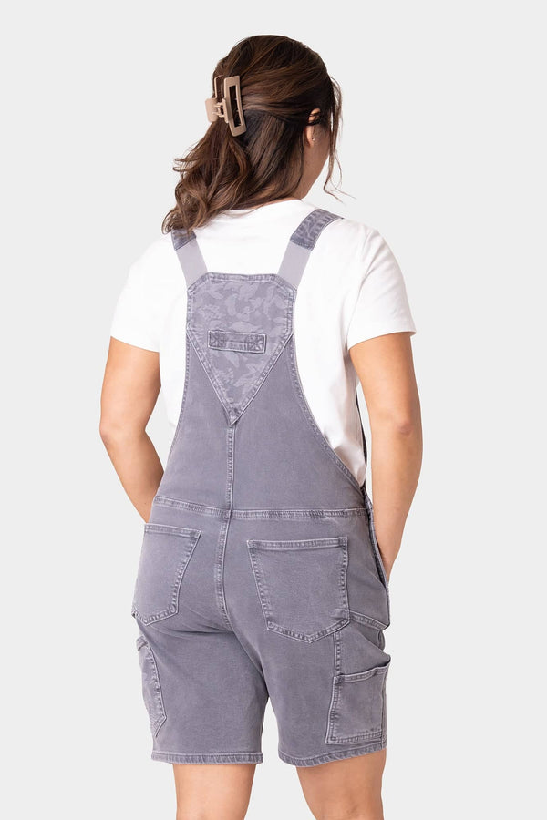 Back view of Dovetail Workwear's Utility Short Overalls in Driftwood Grey, showing nested side pockets, tool loops, and relaxed fit garment-washed denim shortalls on a woman