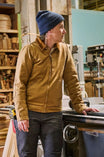Woman wearing the Dovetail Workwear Old School Trucker Canvas Work Jacket in Vintage Brown with a blue beanie, standing in a workshop next to machinery