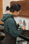 Back view of woman wearing Dovetail Workwear GO TO™ Graphic Hoodie in Lodge Green, showcasing reinforced elbows and custom back graphic design