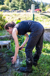 Woman bending forward wearing Dovetail Workwear Provisions Lightweight Ripstop Cargo Pant in Faded Black, demonstrating the pants' flexibility and durability during outdoor work