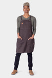 Woman wearing the Dovetail Workwear Obana Work Apron in Kodiak Brown with cross-back straps, displaying multiple pockets and tool organization features
