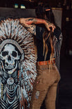 Back view of a woman wearing Dovetail Workwear Rae Ripple X NoSo Patch in tan cargo pants, displaying peel-and-stick patches on denim and artwork beside her