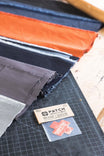Dovetail Workwear x NoSo DIY Repair Patches displayed on a cutting mat, showing multiple fabric patches in paprika orange, indigo denim, black, and grey canvas with adhesive backing