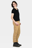 Side view of a woman wearing Dovetail Workwear GO TO™ Stretch Canvas Pant in Sawdust Brown with visible nested pockets and cuffed inseam, paired with a black v-neck tee and black boots