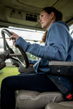 Woman wearing the John Deere X Dovetail Workwear Early Bird Hoodie in Steel Blue while driving, showing the ponytail slit and thumbhole details