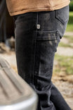 Back view of a woman wearing John Deere X Dovetail Workwear Into Town Bootcut Jeans in Classic Black, highlighting reinforced back pockets and thigh device pocket