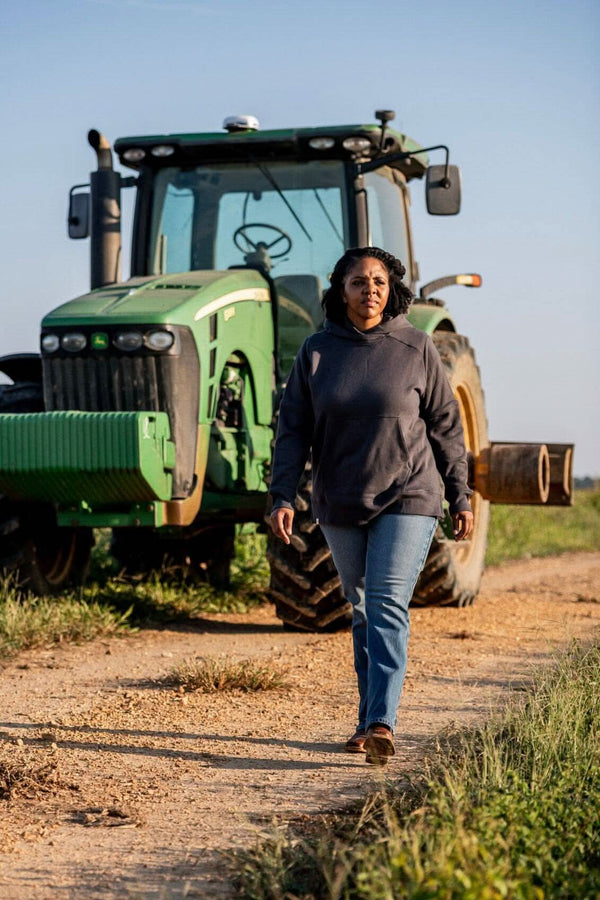 Woman jogging in a Steel Grey John Deere X Dovetail Workwear Early Bird Hoodie on a rural dirt road with a green tractor in the background