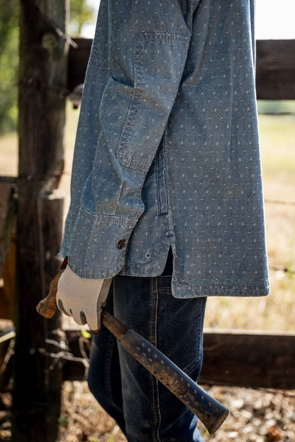Detail view of the John Deere X Dovetail Cultivator Work Shirt in indigo blue dobby, showing reinforced elbows and sun shield cuffs on a woman's arms