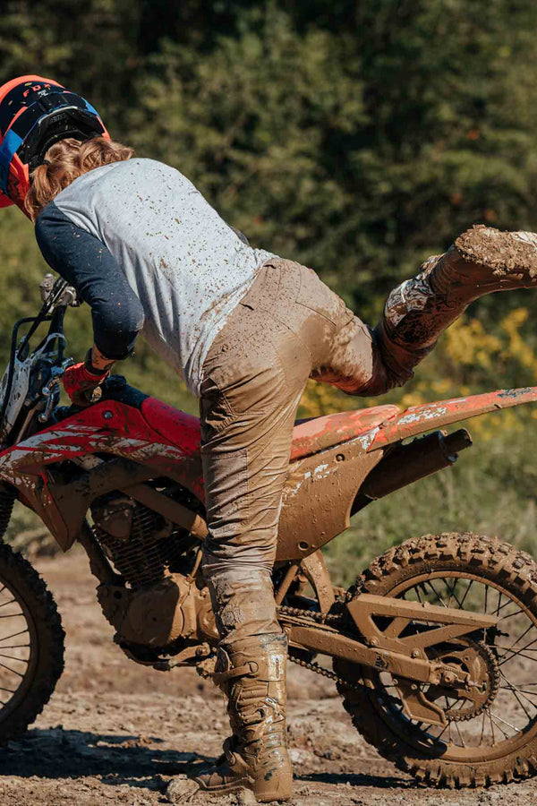 Woman wearing Dovetail Workwear's Britt X Ultralight Work Pant in Flax Ripstop while doing muddy outdoor work, demonstrating the reinforced knees and durability of the cargo-style pants