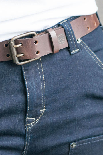Detail view of the Double Pronged Work Belt by Dovetail Workwear in Brown Clay leather, showing the double-pronged buckle and full-grain buffalo leather construction on dark denim jeans