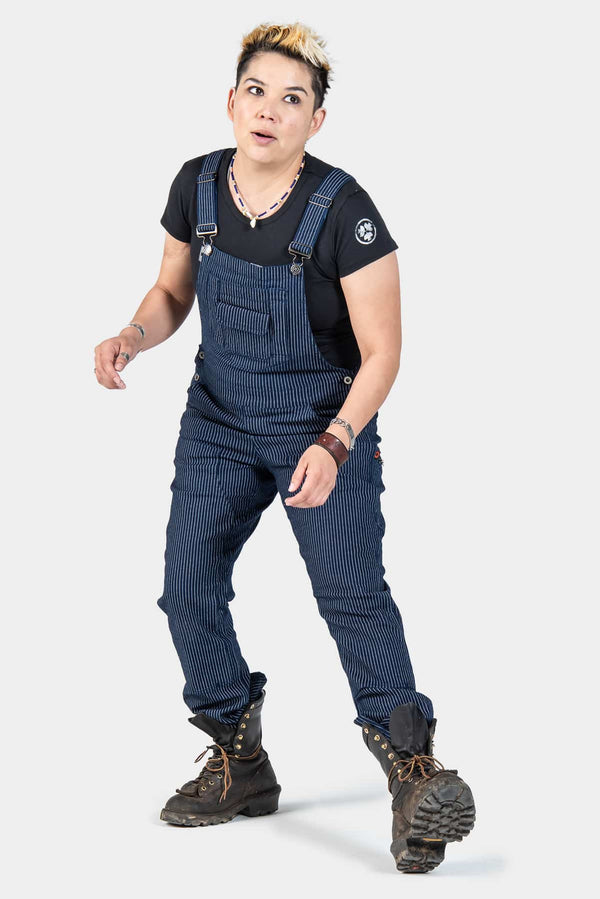 Freshley Overalls in Wabash Stripe by Dovetail Workwear shown on a woman wearing dark boots, featuring visible suspenders, nested pockets, and reinforced knees