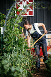 Woman wearing Dovetail Workwear's Freshley Drop Seat Overalls in Navy Canvas while gardening, demonstrating the reinforced knees and tool loops during outdoor work