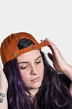 Vintage Paprika Shop Cap by Dovetail Workwear with adjustable strap, shown on a woman wearing the cap tilted back
