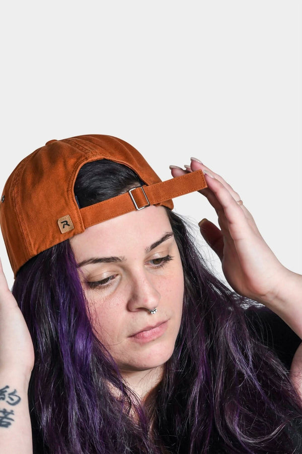 Vintage Paprika Shop Cap by Dovetail Workwear with adjustable strap, shown on a woman wearing the cap tilted back