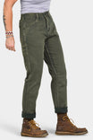 Side view of a woman wearing Dovetail Workwear's Shop Pant in Olive Green Denim, cuffed at the ankles, paired with brown work boots