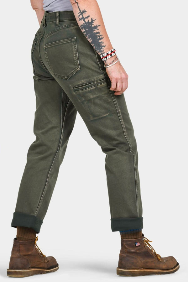 Back view of a woman wearing Dovetail Workwear's Shop Pant in Olive Green Denim, featuring visible cargo pockets, crotch gusset, and rolled cuffs with brown boots
