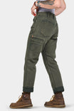 Back view of a woman wearing Dovetail Workwear's Shop Pant in Olive Green Denim, showcasing cargo pockets and crotch gusset detail, cuffed and paired with brown work boots