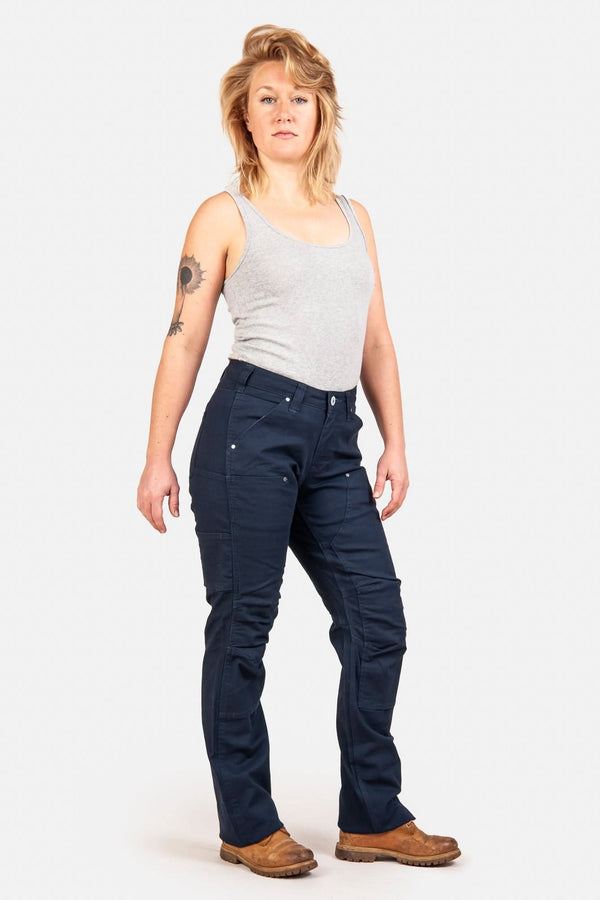 Anna Taskpant in Uniform Navy Canvas by Dovetail Workwear, shown on a woman in a gray tank top, featuring Hip Slot™ Tool loop, Nested Pockets, reinforced knees, and a straight leg silhouette