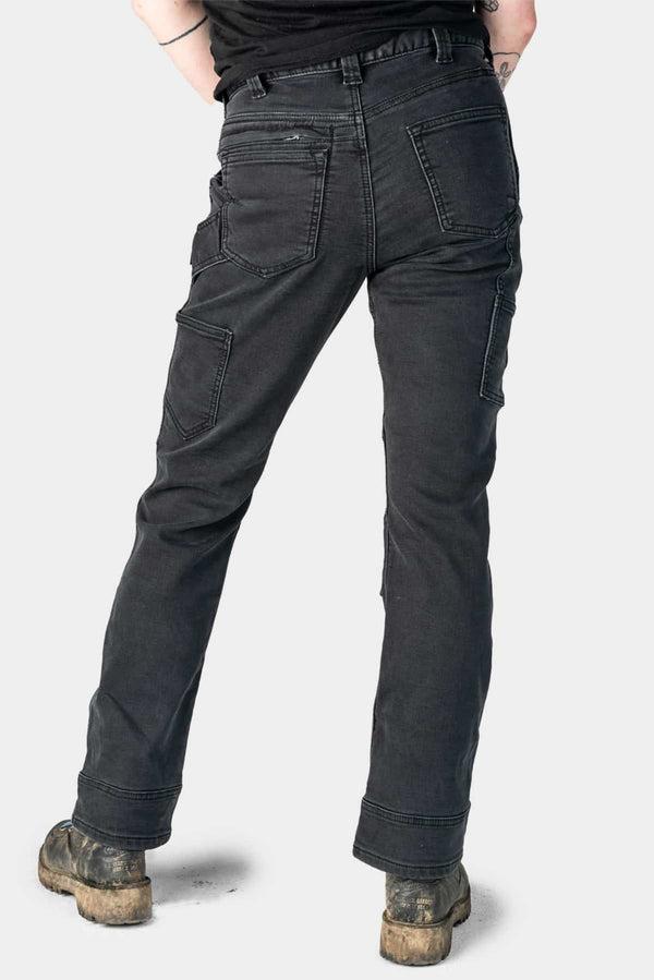 Back view of a woman wearing Dovetail Workwear Britt Utility Pant in Black Stretch Thermal Denim, showing cargo-style pockets, reinforced knees, and rolled cuffs with work boots