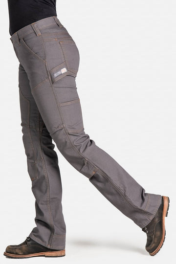 Side view of a woman wearing Dovetail Workwear's Britt Utility Pant in FR Grey Canvas, showcasing cargo-style pockets, reinforced knees, and straight leg fit with brown boots