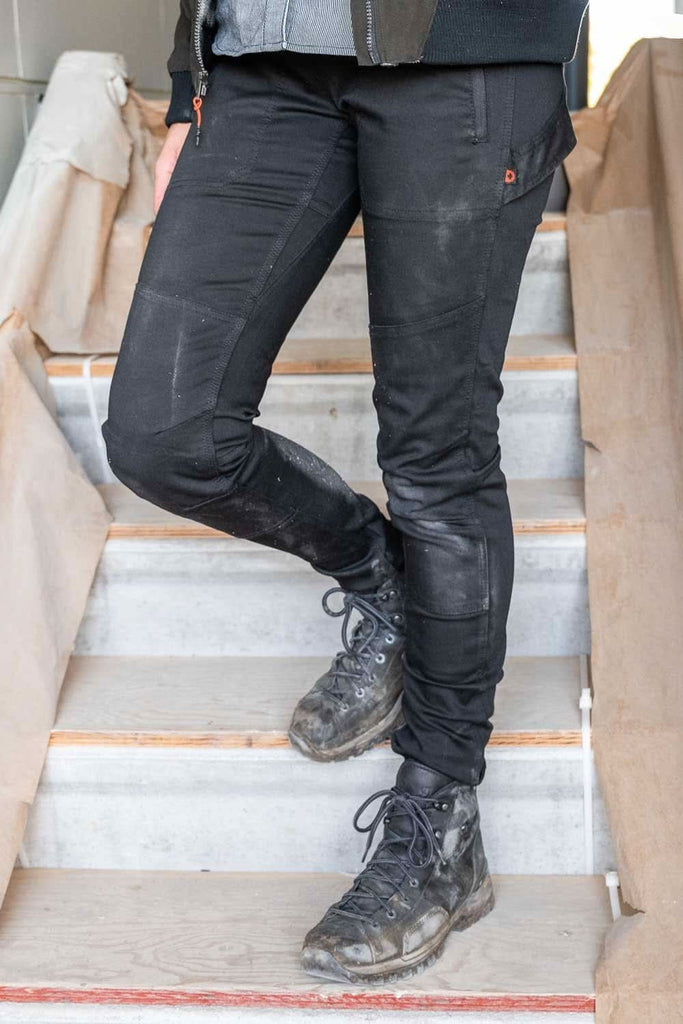 Woman climbing stairs wearing Dovetail Workwear Christa DIY Pant in Black Performance Modal with reinforced knees and lace-up boots