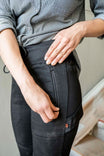 Detail view of the Christa DIY Pant in Black Performance Modal by Dovetail Workwear, showing a woman's hands demonstrating the nested pocket and tool loop features